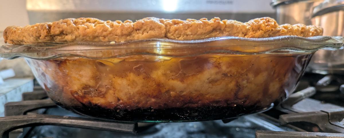 A baked apple pie viewed from the side through a glass pan, with the bottom part looking blackish.