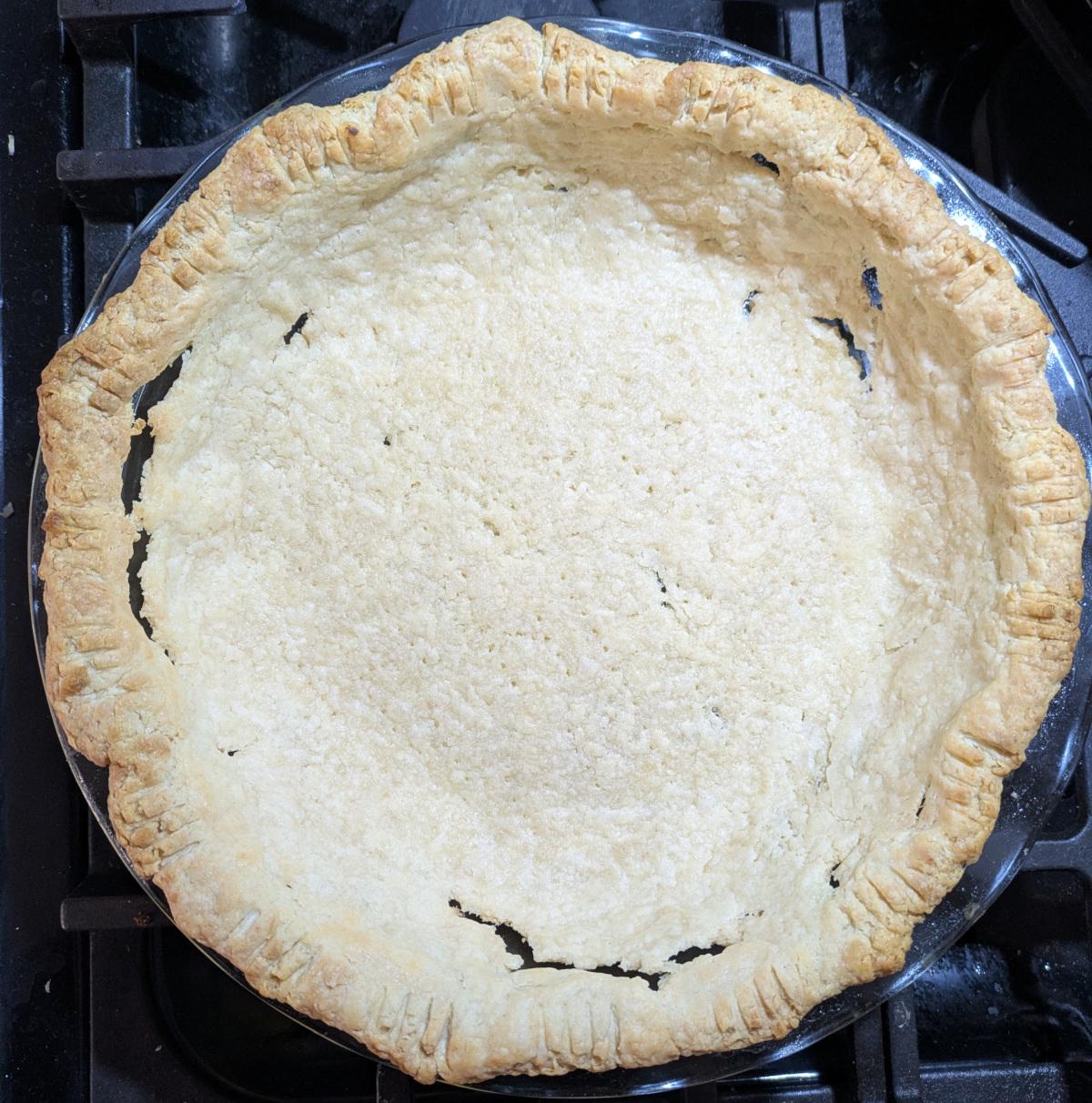 An empty baked pie crust with some holes around the sides that appeared during baking.
