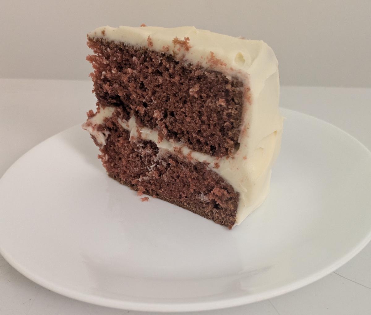 A slice of red velvet cake with white cream cheese frosting on the top, outside, and between the two layers.