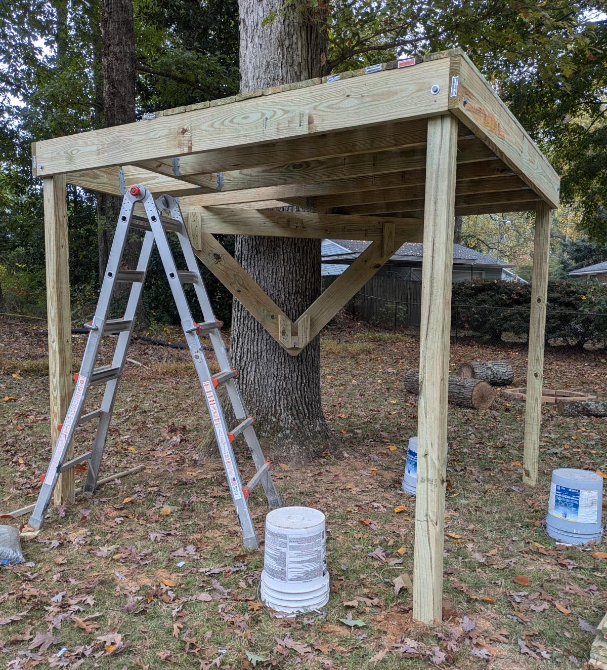 The platform with the joists complete and the right half of the decking in place, shown from below. The decking runs parallel to the joists. A folding ladder stands by the trap door opening.